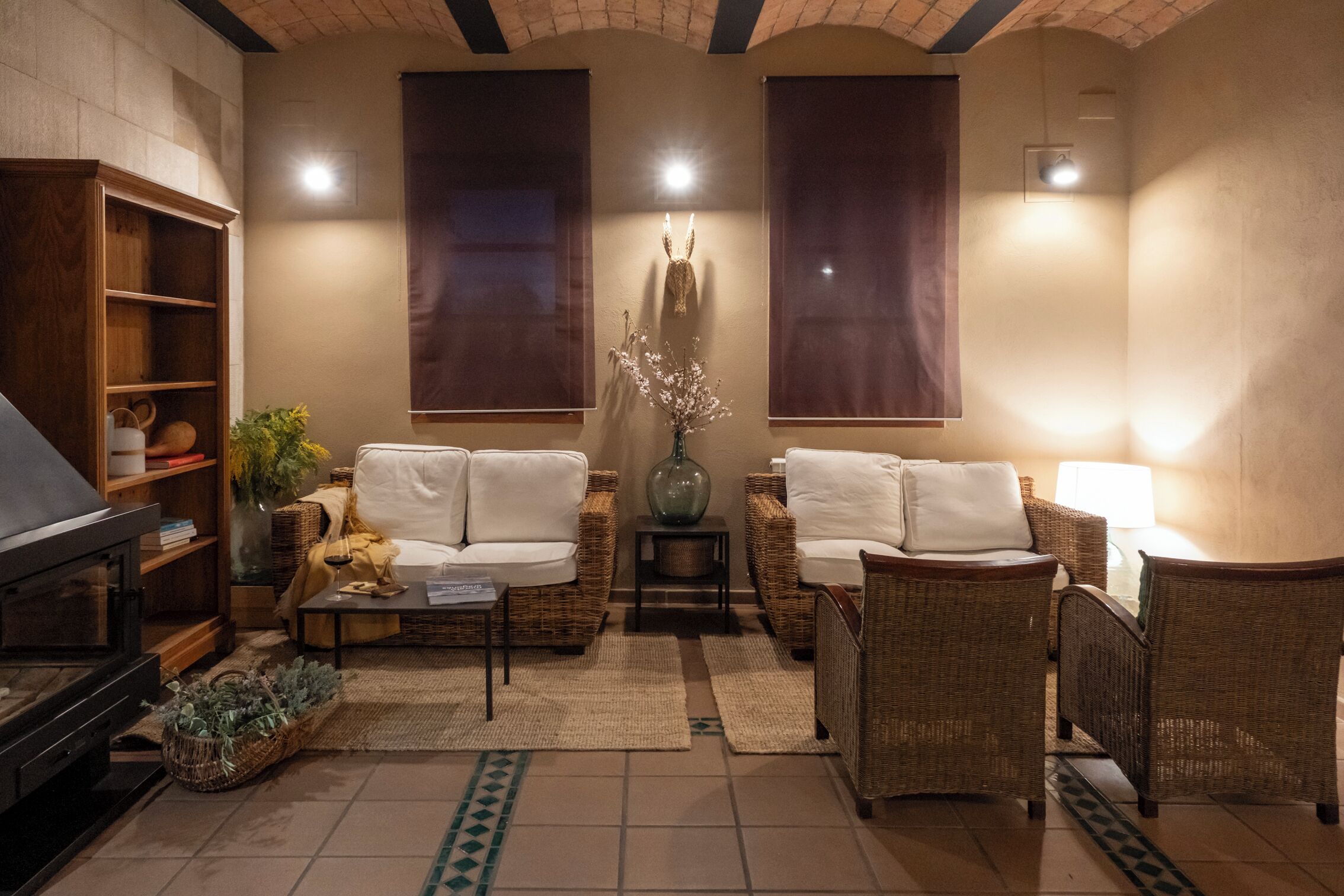 Una sala de estar acogedora con chimenea, muebles de mimbre y un jarrón grande con flores.