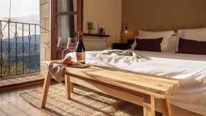 Un dormitorio con una cama grande, un banco de madera, una botella de vino y copas sobre una mesa.