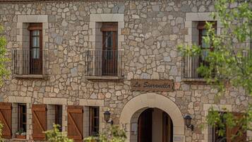 A stone building with a tiled roof, named "La Siuranella." It features multiple windows with wooden shutters, a central arched entrance, and a balcony with metal railings.