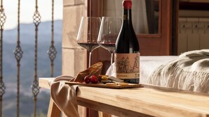 Una mesa de madera con una botella de vino, copas y un plato de queso y uvas.