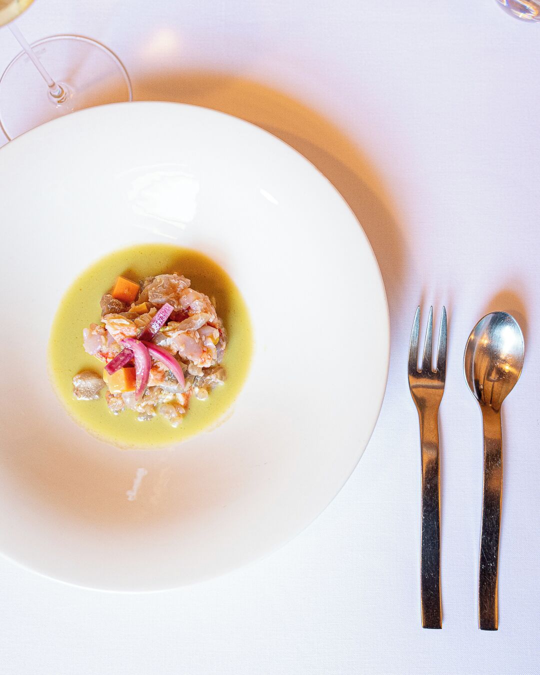 Une assiette blanche contenant un plat de fruits de mer, accompagnée d’une fourchette et d’une cuillère, le tout posé sur une nappe blanche.
