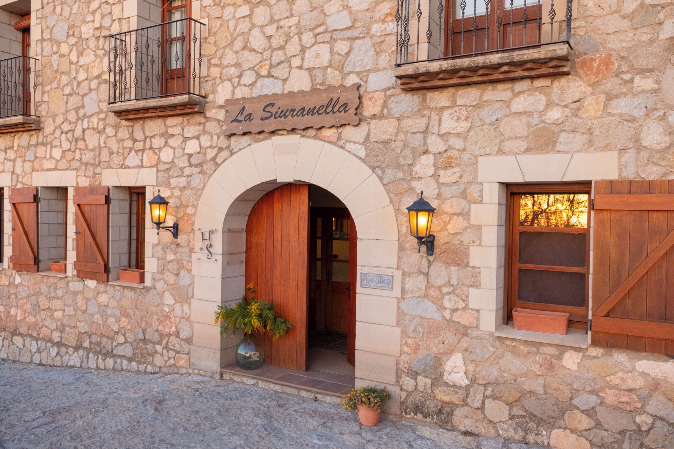 A stone building with an arched entrance, wooden shutters, and a sign reading "La Siuranella".