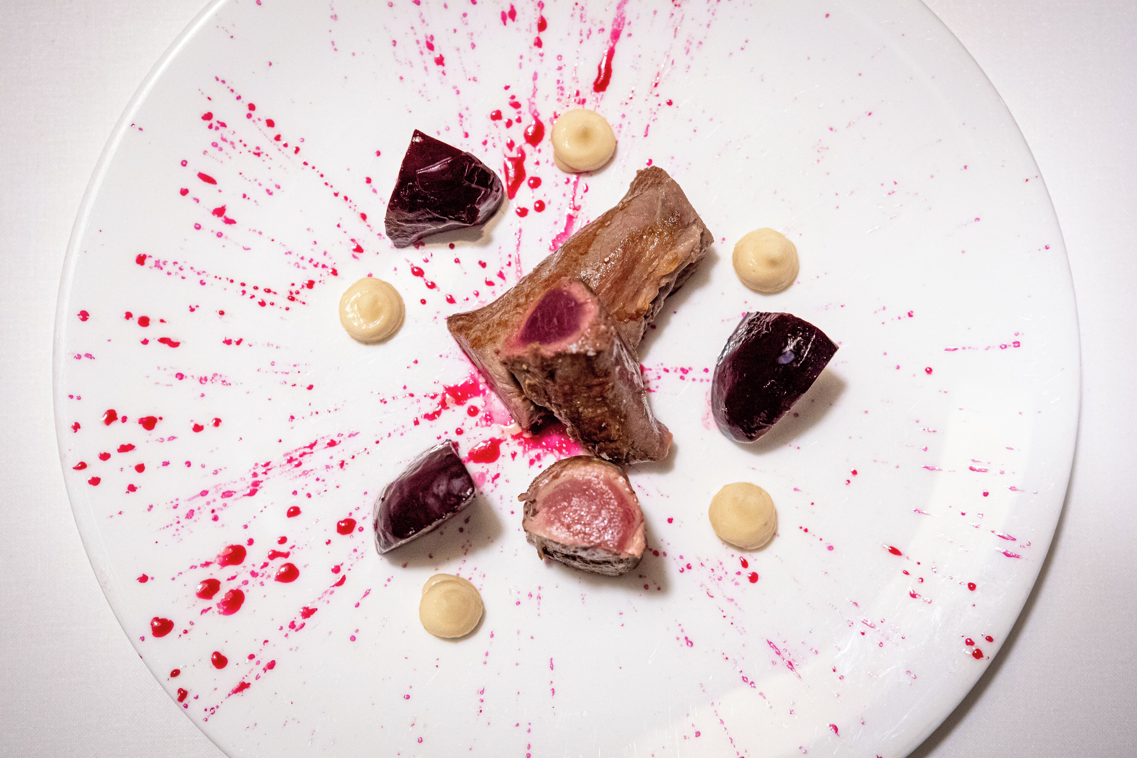 A white plate with a piece of meat and several small round items, possibly condiments or garnishes.