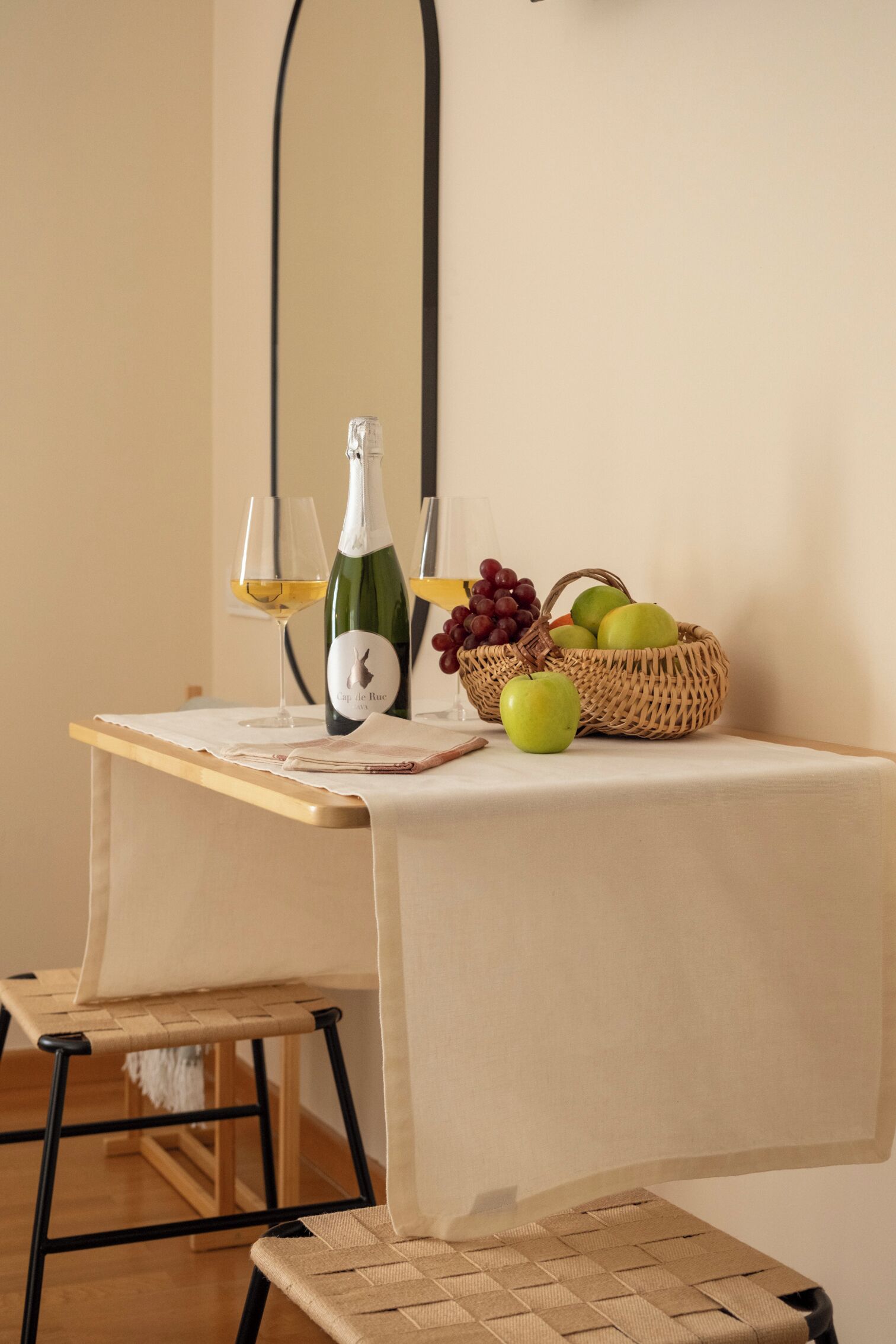 A table with a bottle of wine, glasses, and a basket of fruit.