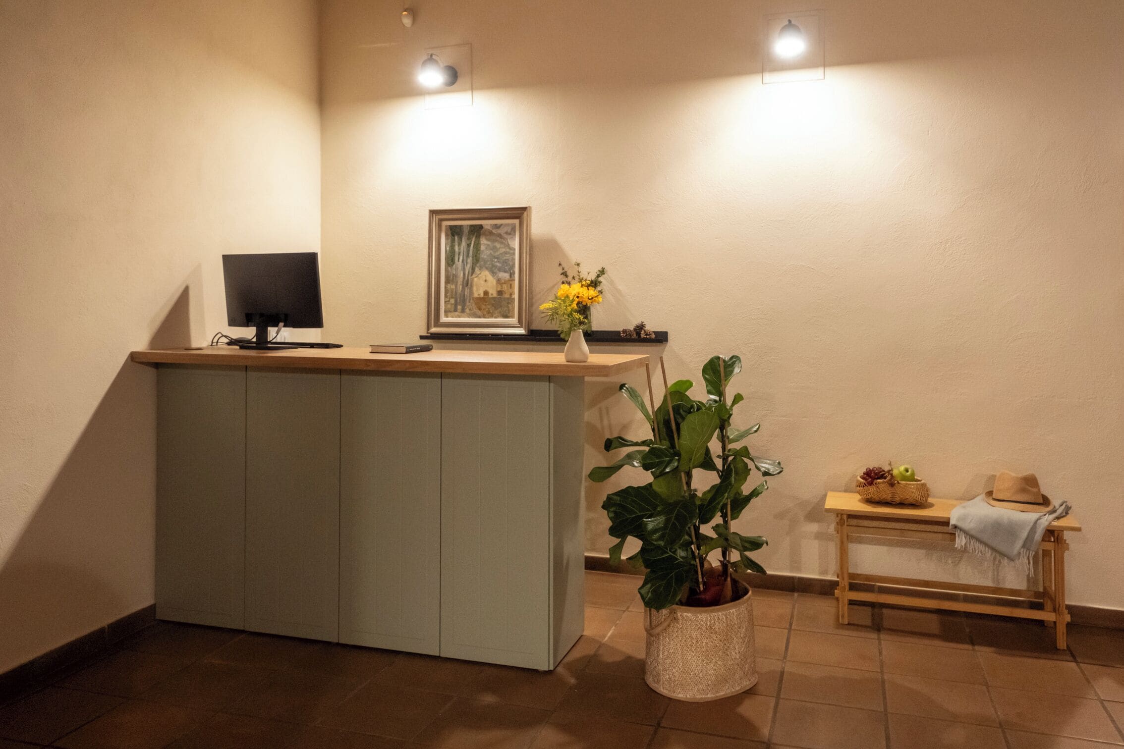Een receptiebalie met een computer, ingelijste kunstwerken en een potplant.