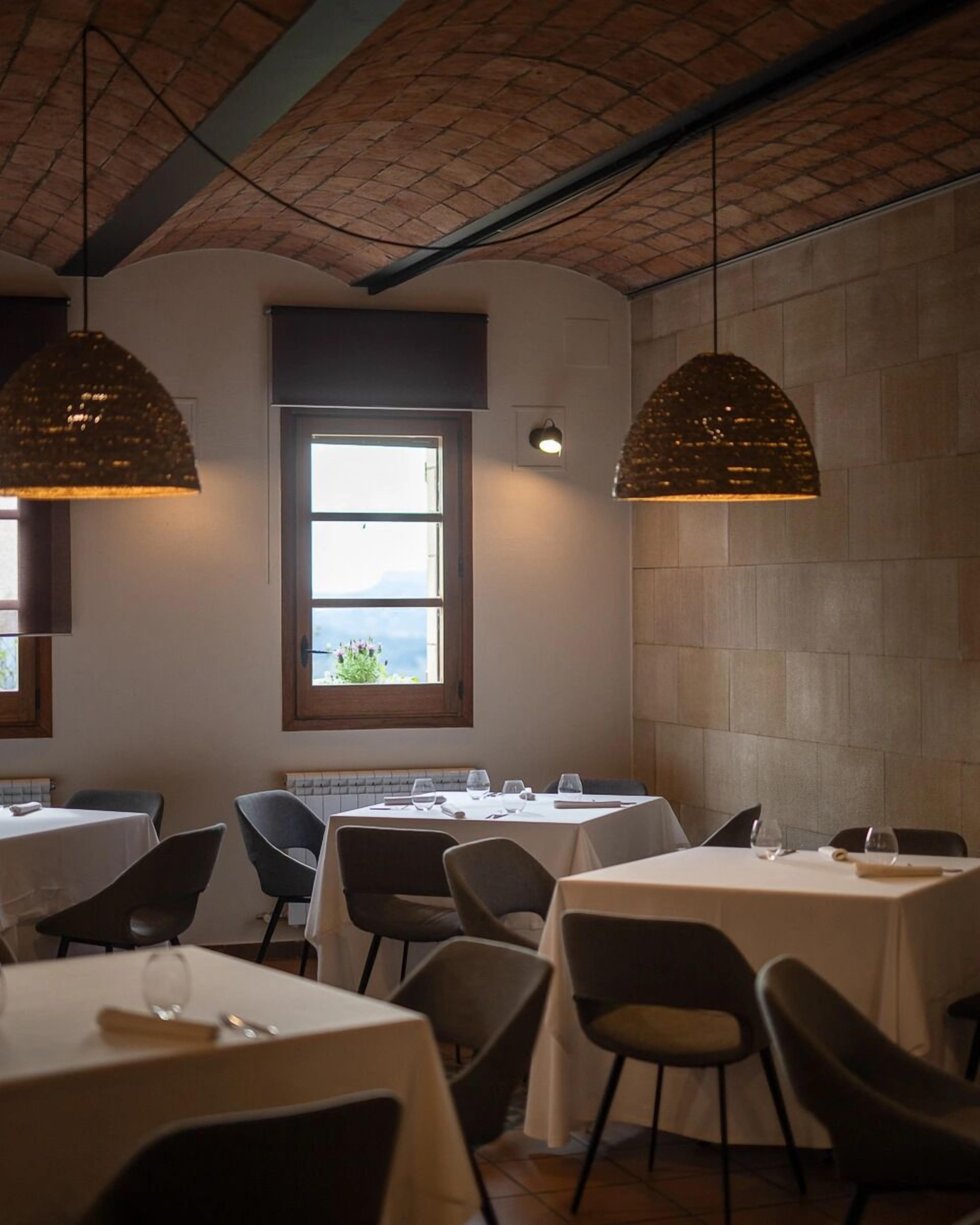 Ein Restaurant mit mehreren Tischen und Stühlen, einem großen Fenster mit Blick und hängenden Pendelleuchten.