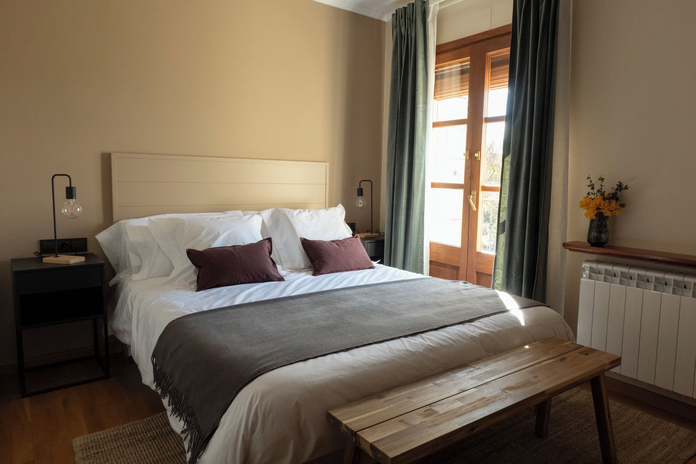 A neatly arranged bedroom with a bed, bedside tables, a bench, and a window with curtains.