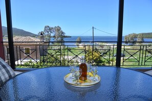 Ein Glastisch mit einer Flasche und Gläsern auf einer Ablage, mit Blick auf eine malerische Wasserlandschaft und viel Grün.