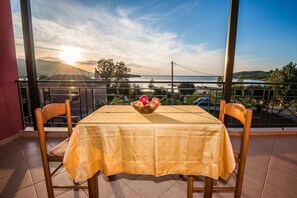 Ein Tisch mit Tischdecke und Stühlen auf einem Balkon mit Blick auf ein Gewässer und hügelige Landschaft bei Sonnenuntergang.