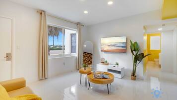 A modern living room with a sofa, two round tables, a TV, and a large window with curtains.