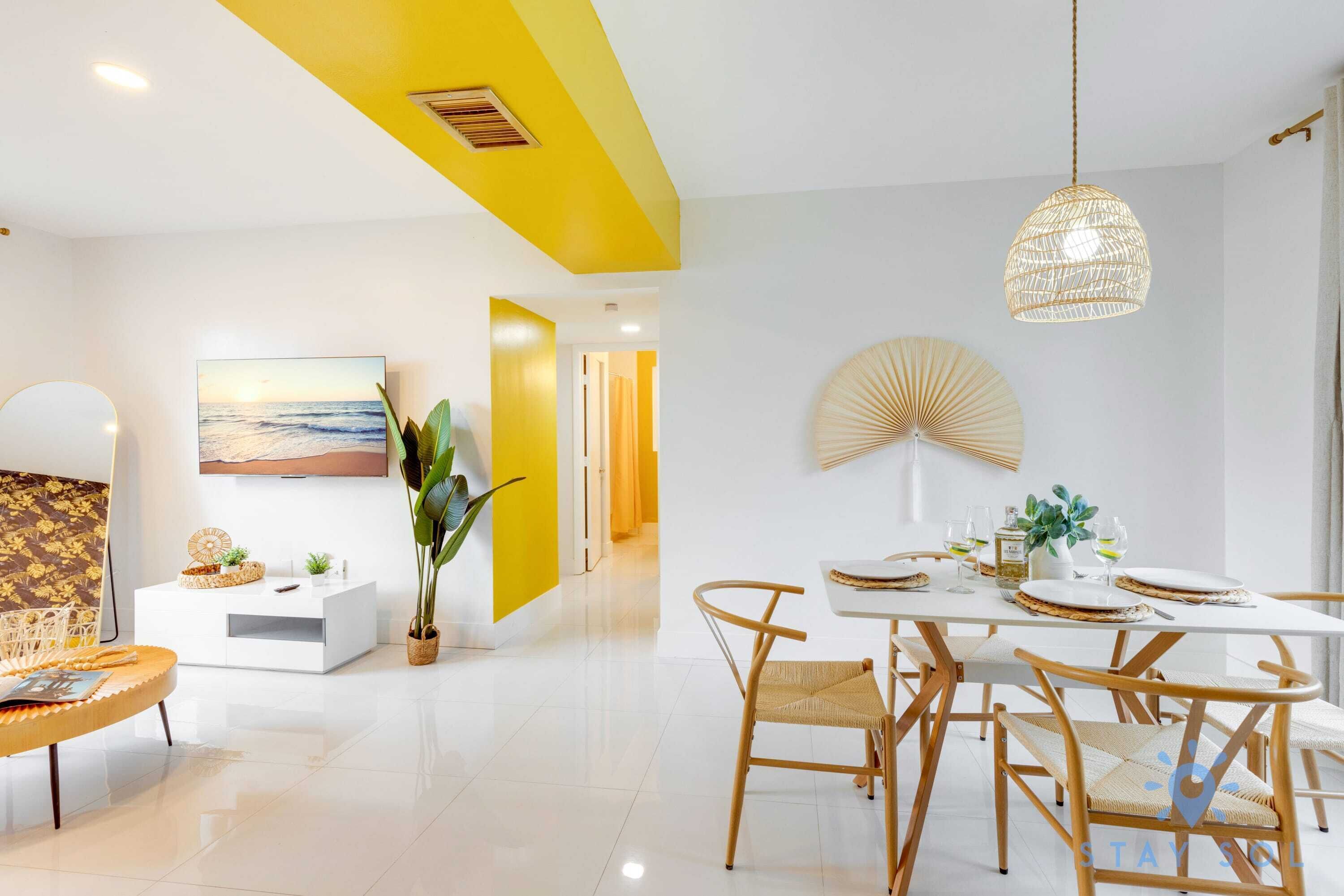 Een moderne eetruimte met een witte tafel voor vier personen, omringd door rieten stoelen.