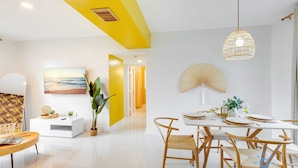 Un espace repas moderne avec une table blanche dressée pour quatre personnes, entourée de chaises en osier.