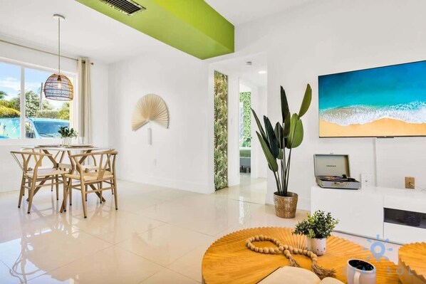 A modern living room with a dining area, a large window with a view of a pool, and a TV on the wall.