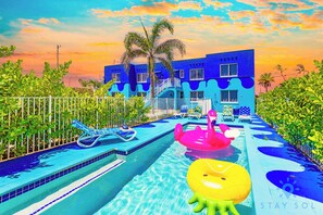 A swimming pool with inflatable toys, a white fence, and a building with blue walls.