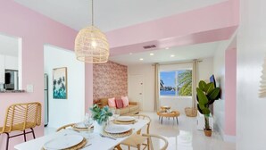 A modern dining area with a white table set for four, a wicker pendant light, and a view of the outdoors through a large window.