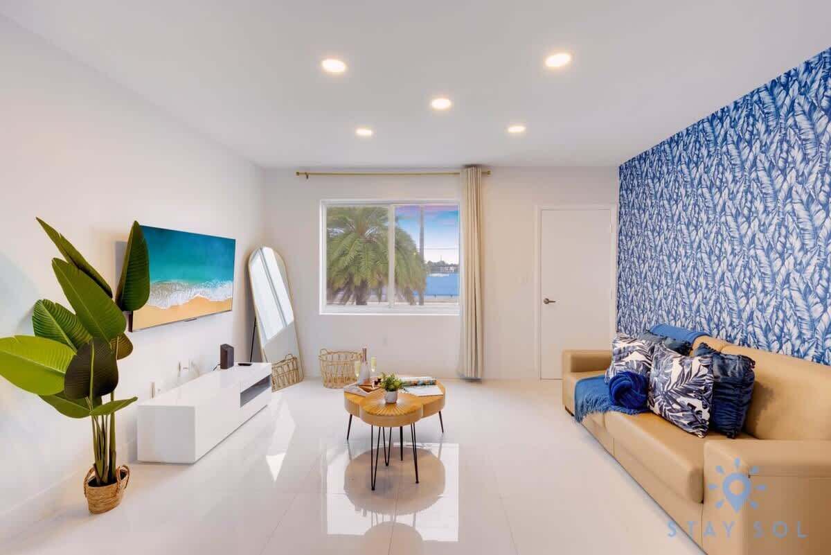 Una sala de estar moderna con un sofá blanco, una mesa de centro y un ventanal con vistas a palmeras.