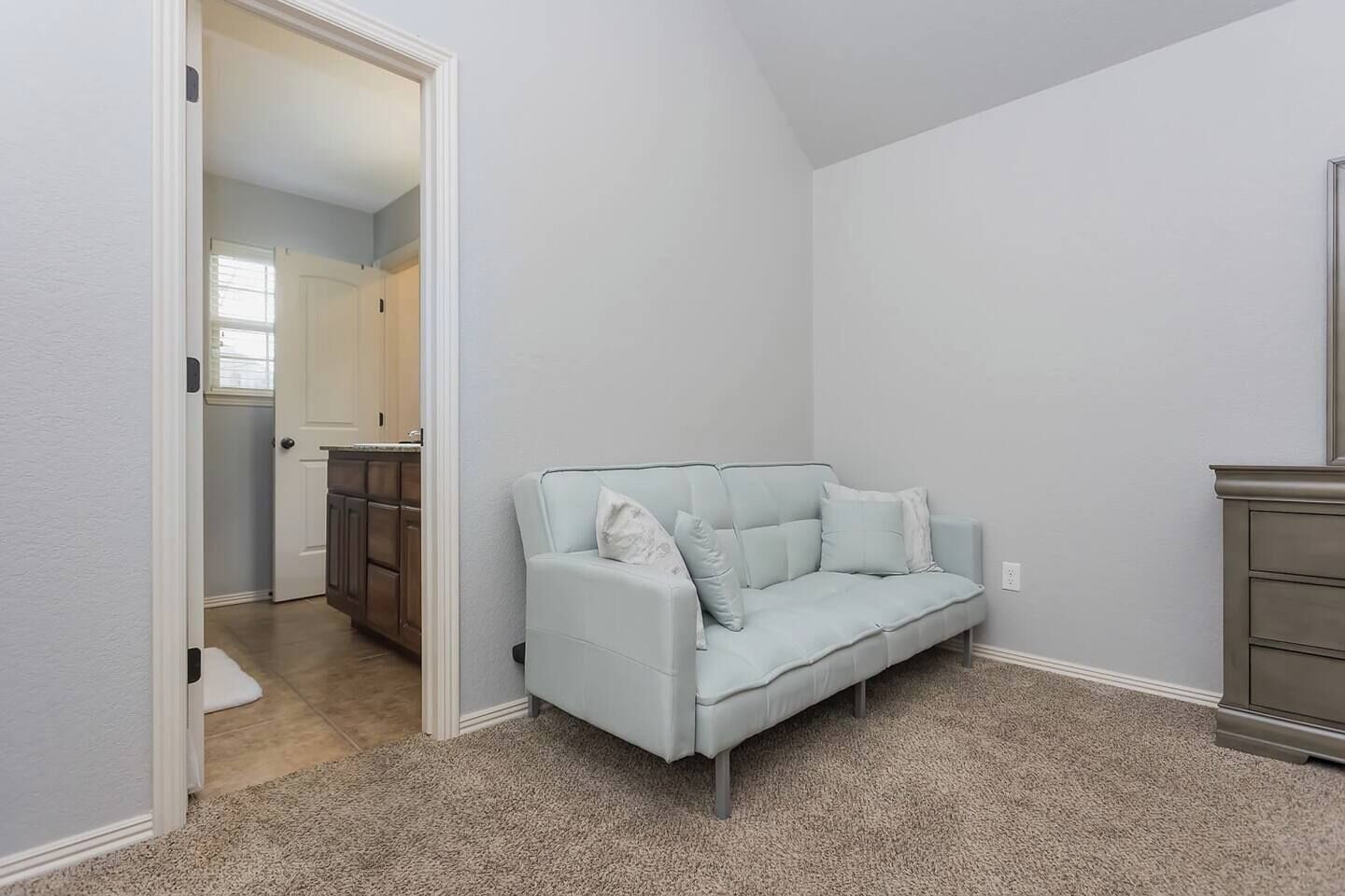 Una habitación con un sofá azul claro, un armario de madera y suelo alfombrado.