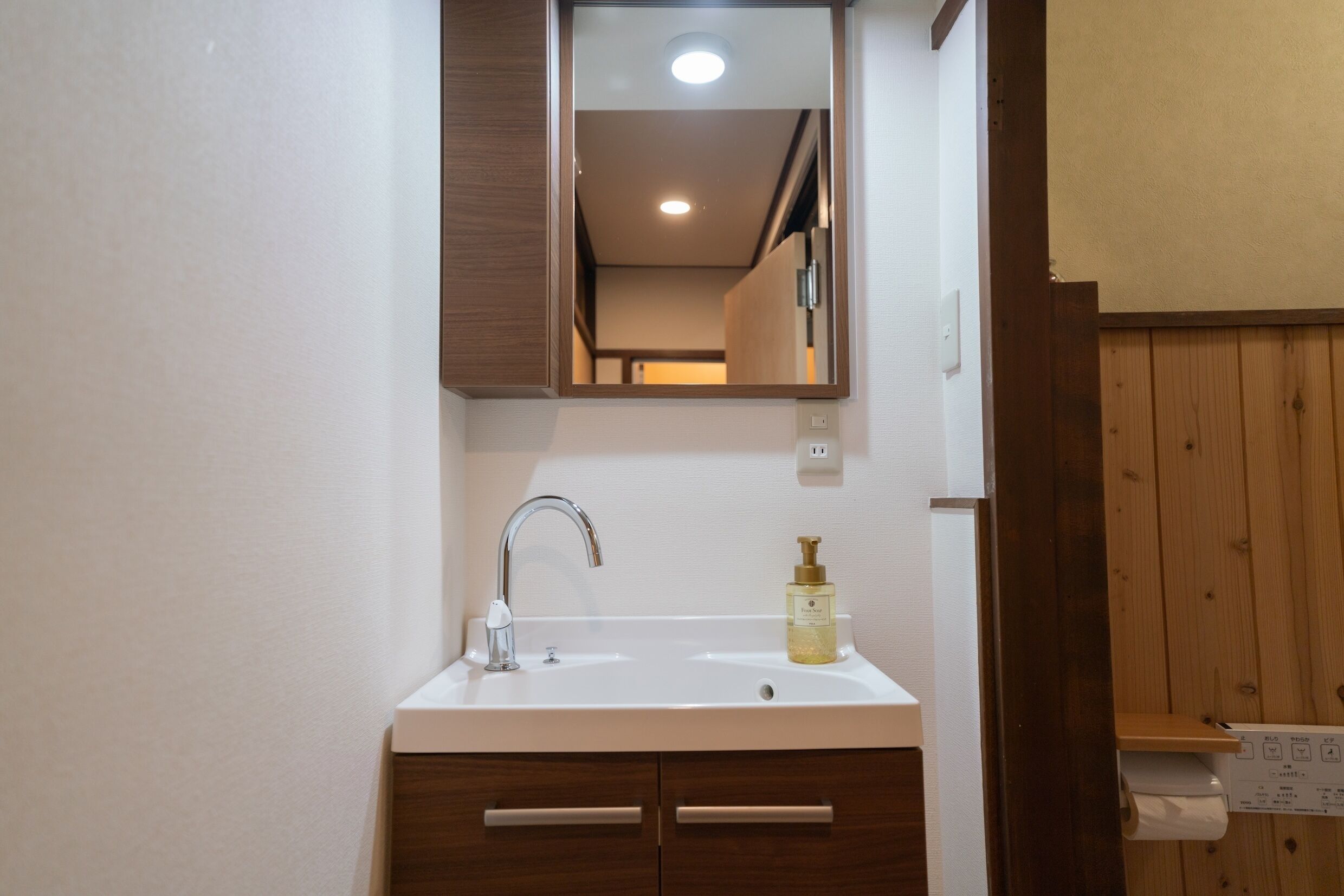Une salle de bain avec un lavabo blanc, des meubles en bois, un miroir et un panneau mural en bois.