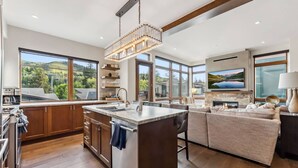 A modern kitchen with a large island, wooden cabinets, and a view of the outdoors. - LUXE Riverfront Mountain Retreat | Walk to Gondola (Avon)