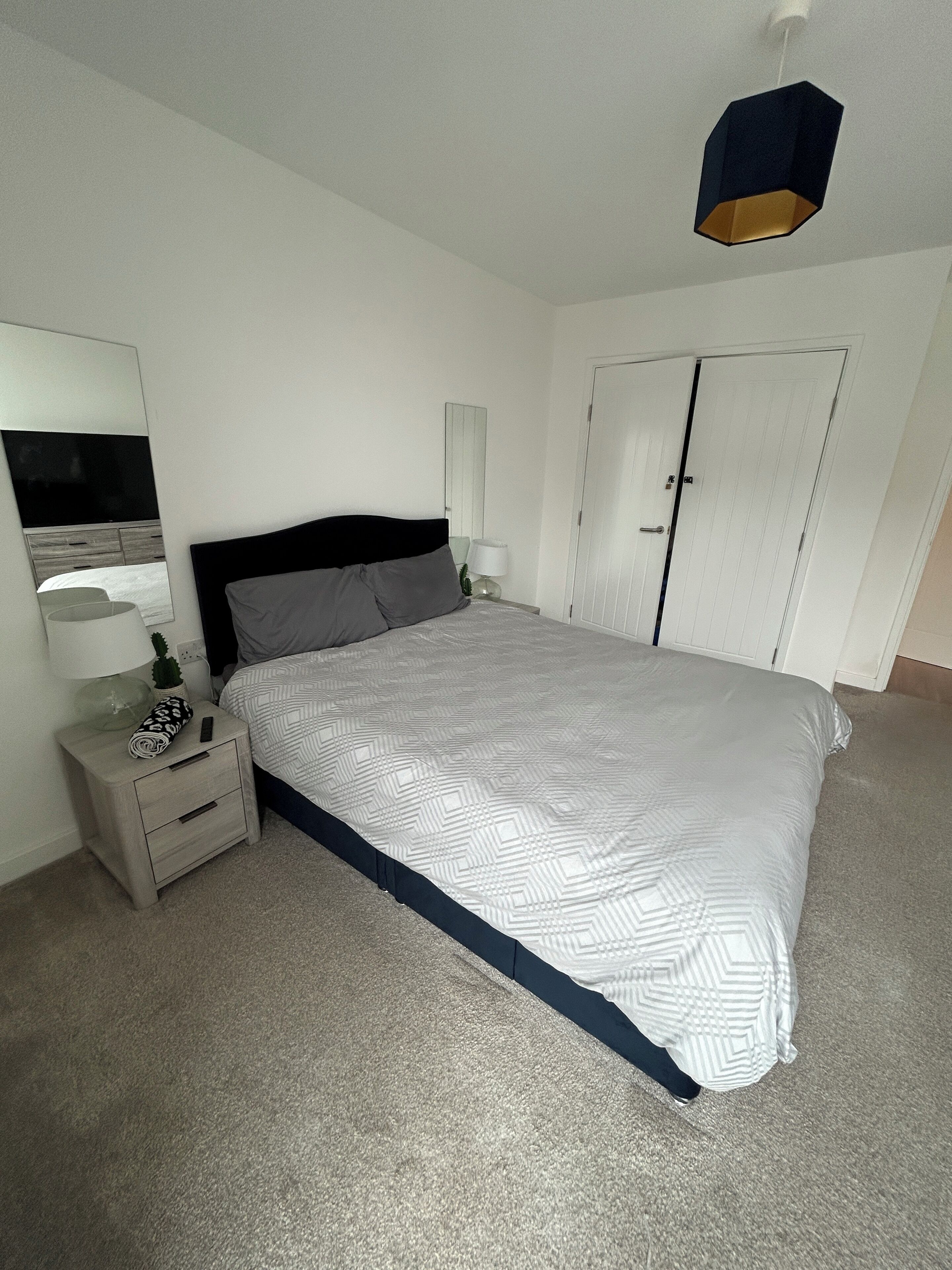 Ein Schlafzimmer mit einem Bett, Nachttischen, einer Lampe, einem Spiegel und einem Kleiderschrank.