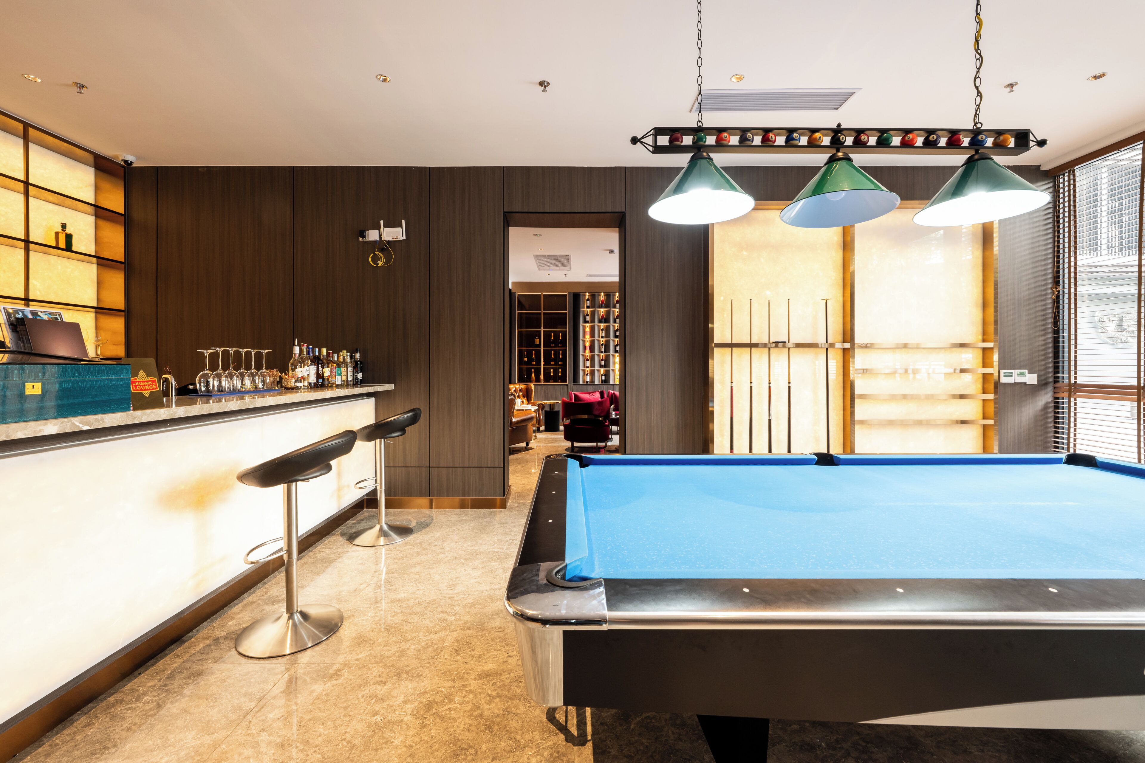 A pool table in a room with a bar area, a seating area, and a view through a door.