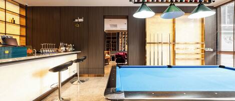 A pool table in a room with a bar area, a seating area, and a view through a door.