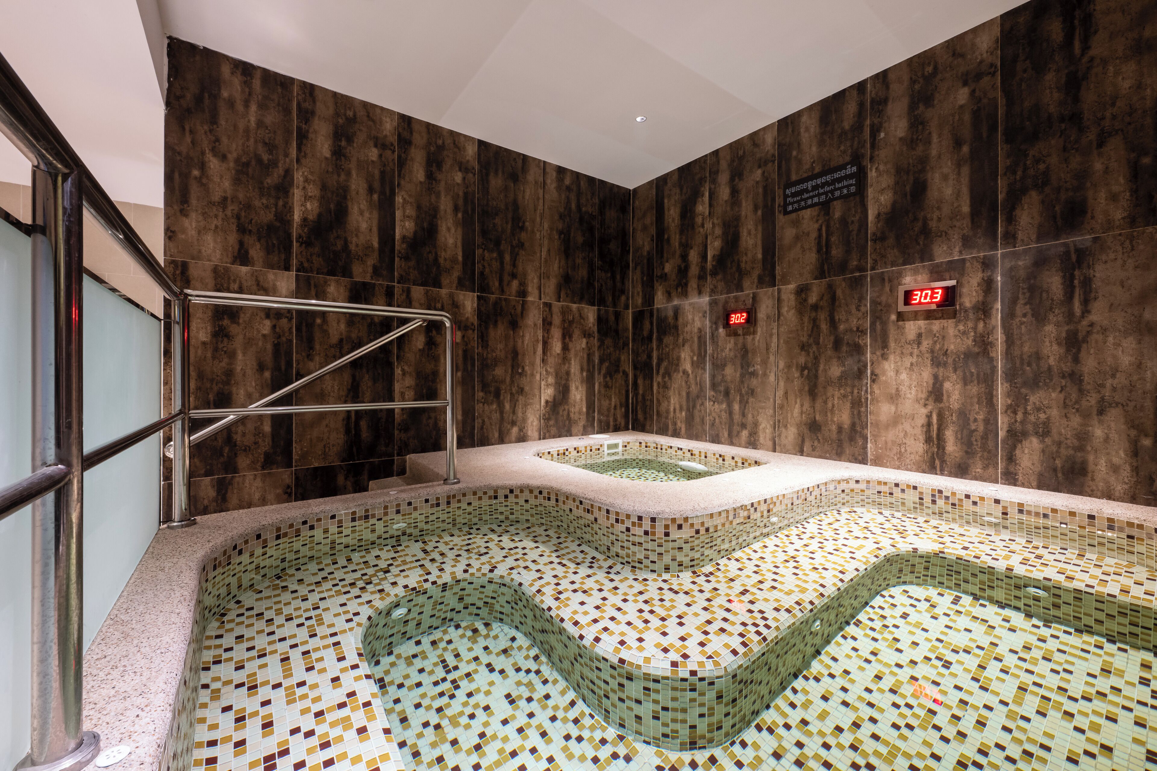 Une piscine intérieure moderne, dotée d’un sol en mosaïque et d’une rambarde métallique.
