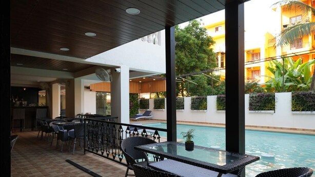 An outdoor seating area with a pool view, featuring a glass table and wicker chairs. - Evoke Express Candolim (Candolim)