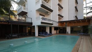 A swimming pool with lounge chairs and a covered area with tables and chairs. - Evoke Express Candolim (Candolim)