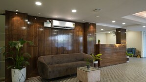 A modern reception area with a wooden reception desk, a sofa, and potted plants. - Evoke Express Candolim (Candolim)