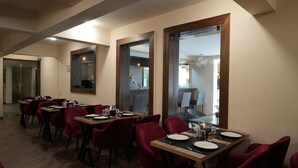 A dining area with tables set for two, red upholstered chairs, and a wooden floor. - Evoke Express Candolim (Candolim)