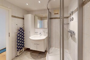 Ein modernes Badezimmer mit einer gläsernen Duschkabine, einem weißen Waschbecken und einem Spiegel darüber.