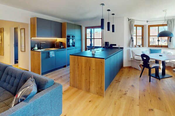Eine moderne Küche mit einer zentralen Kochinsel, Holzboden und einem Essbereich mit Tisch und Stühlen.
