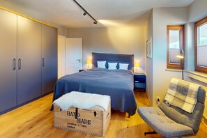 Ein Schlafzimmer mit einem Bett, Nachttischlampen, einer Holzkiste, einem Sessel und einem Kleiderschrank.