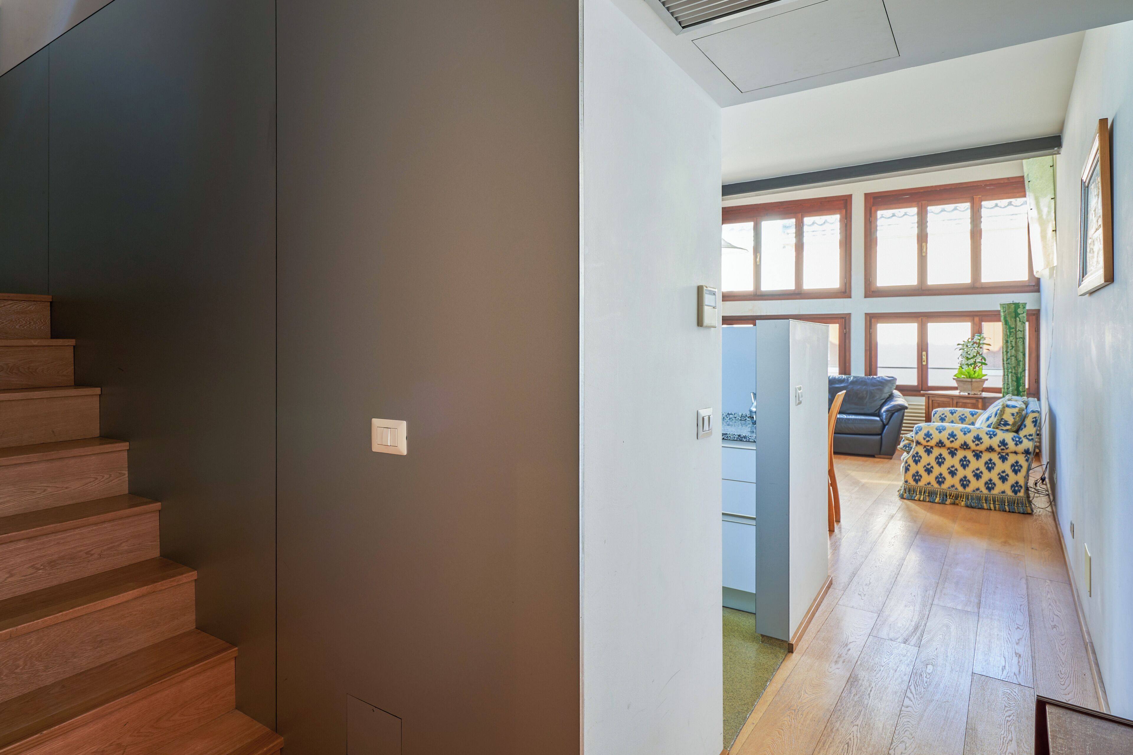 Een trap die leidt naar een kamer met uitzicht op een balkon, een bank en een raam met jaloezieën.