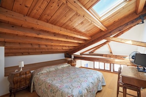 Ein Schlafzimmer mit Holzboden, einem Bett mit floralem Bettbezug, einem Nachttisch mit Lampe und einem Schreibtisch mit Computer.
