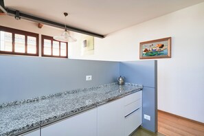 Eine Küche mit Granit-Arbeitsplatten, weißen Schränken, einer Hängeleuchte, einem Bild an der Wand und einem Fenster mit verzierten Gitterstäben.