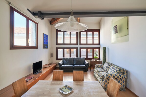 A living room with a sofa, a dining table, and a TV. - Ca' dell'Arte - San Giacomo (Venezia)