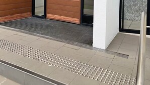 Ein moderner Gebäudeeingang mit Holzfassade, Glastüren und einer Metallstufe.