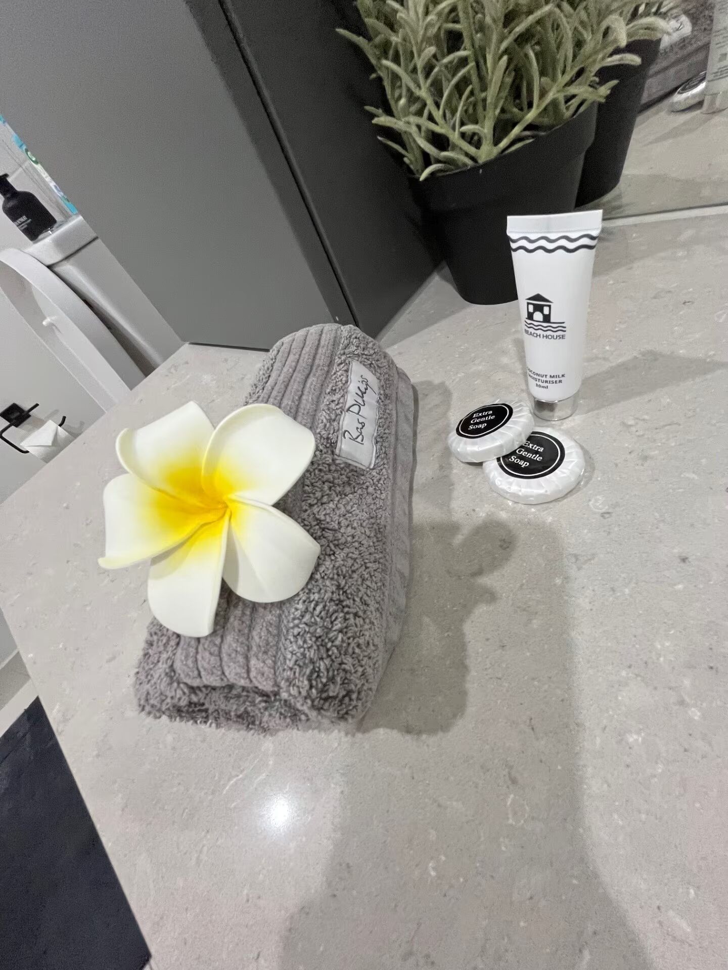Een handdoek met een bloem, een fles kokosmelkzeep en een potplant op een badkamermeubel.