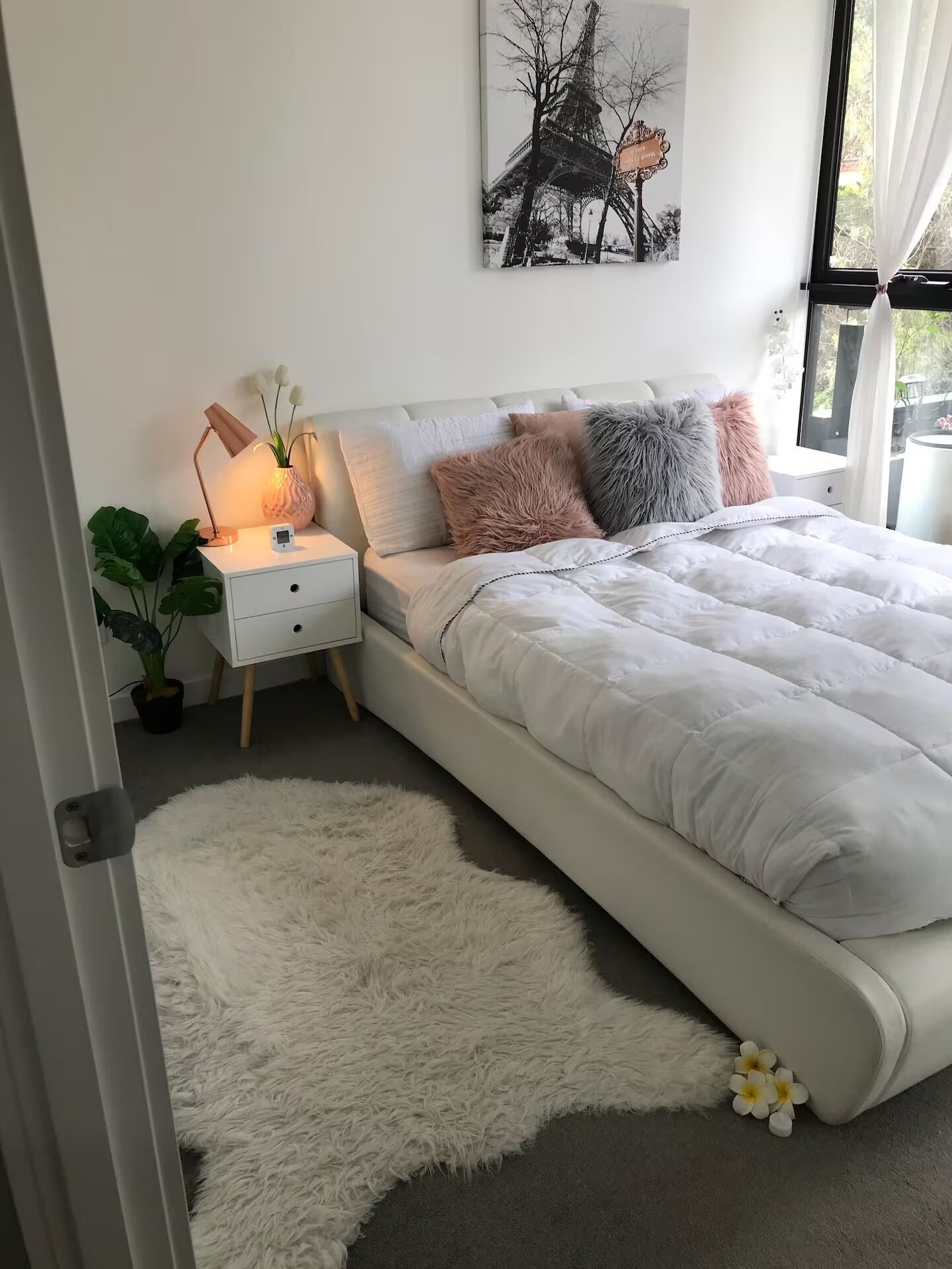 Une chambre avec un lit blanc, des oreillers moelleux, une table de chevet avec une lampe et une grande fenêtre.