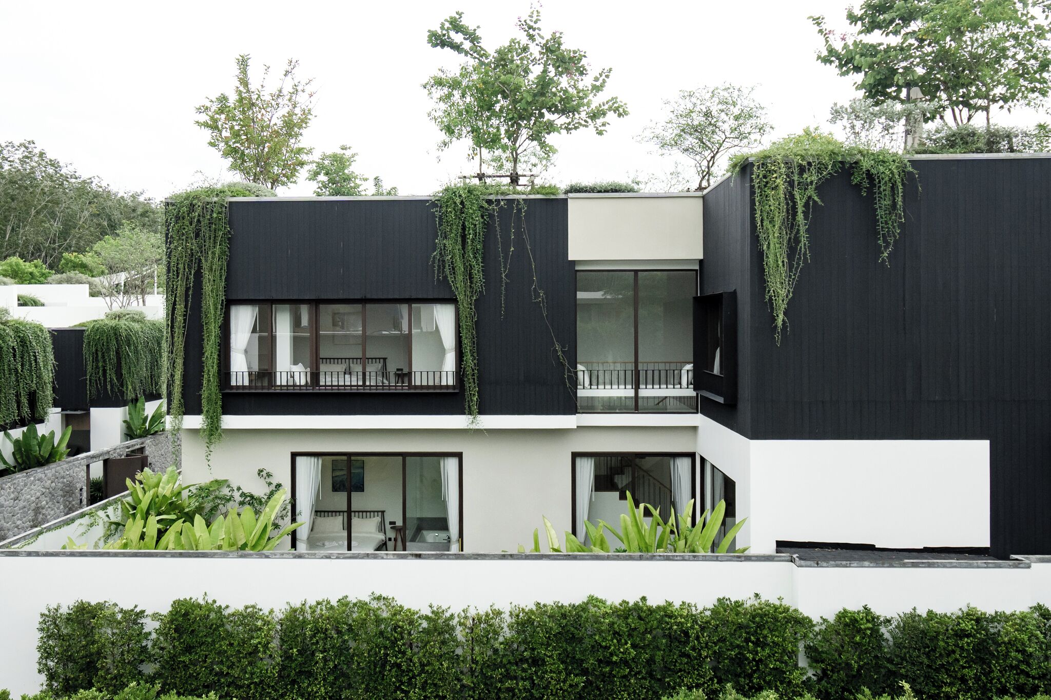 A modern two-story building with a flat roof, large windows, and a balcony with a railing.