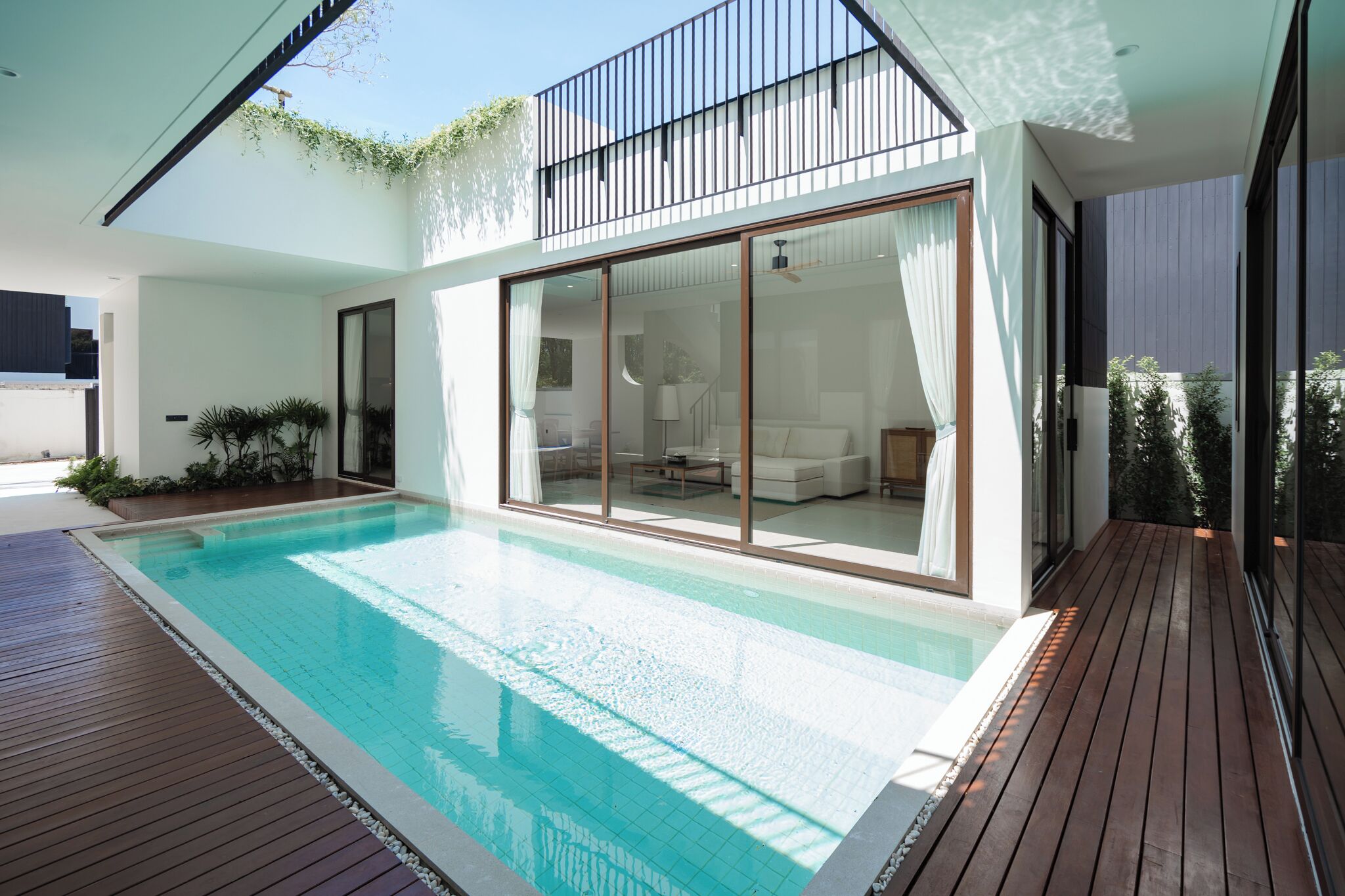Uma casa moderna com piscina, grandes portas de vidro deslizantes e um deck de madeira.