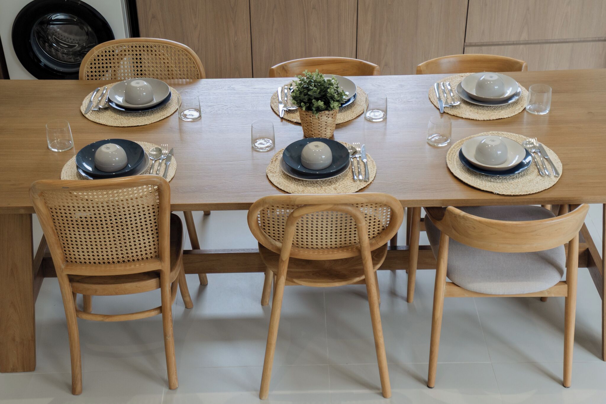 Mesa de jantar de madeira posta com pratos, tigelas, talheres e copos.