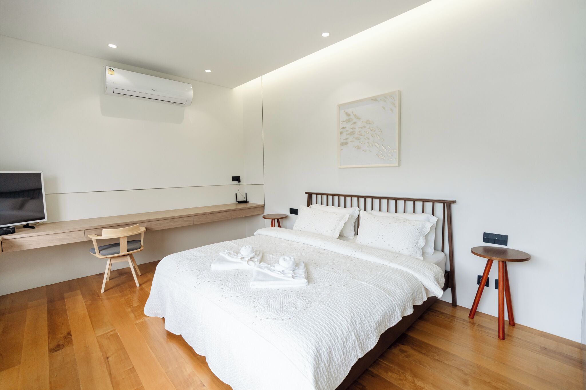 A modern bedroom with a bed, a TV, a desk, and a chair.