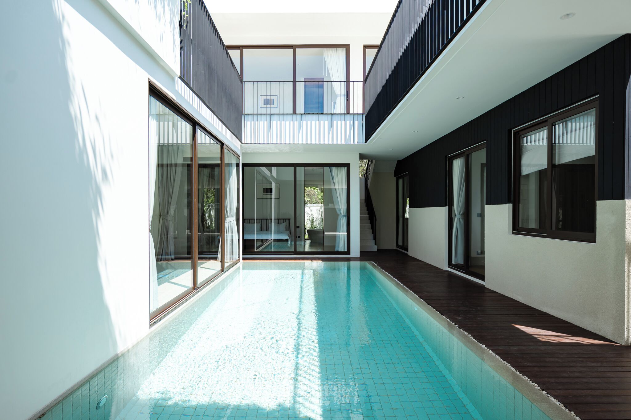 A modern house with a swimming pool, large glass doors, and a balcony.