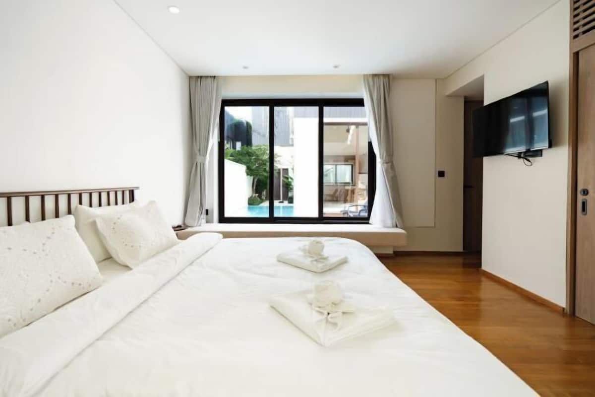 Quarto de hotel com uma cama grande, televisão na parede e vista para uma piscina pela janela.