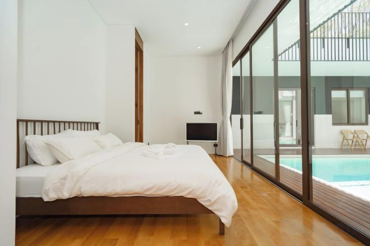 A bedroom with a bed, a TV, and a view of a swimming pool.