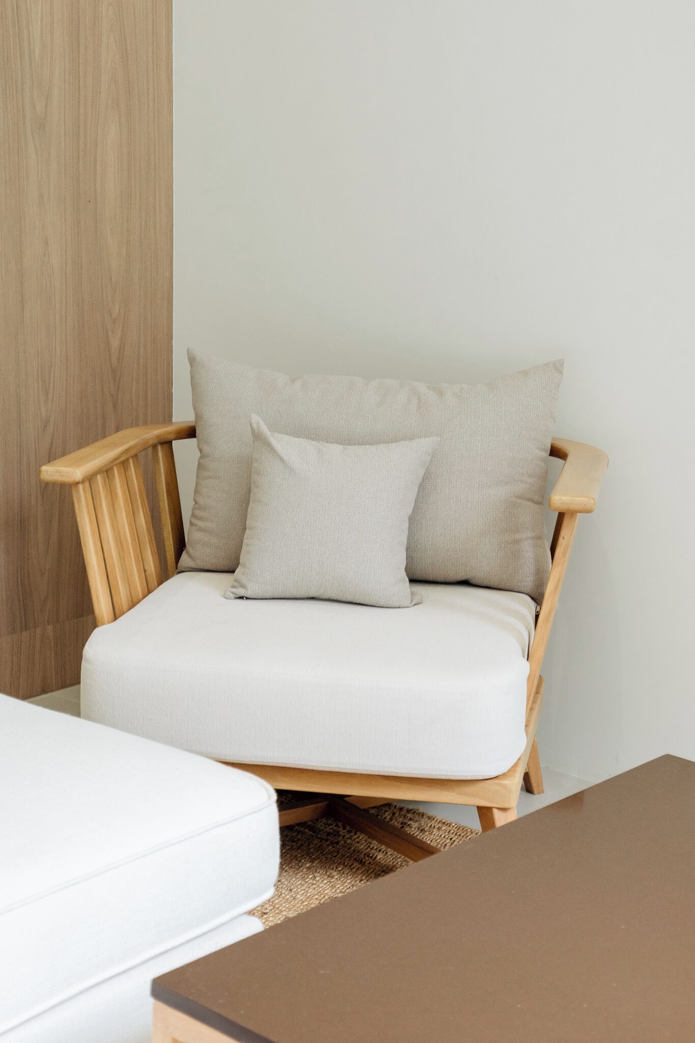 Una silla de madera con un cojín blanco y dos almohadones, apoyada contra una pared lisa.