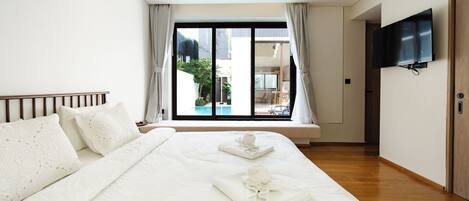 A hotel room with a large bed, a TV mounted on the wall, and a view of a swimming pool through the window.